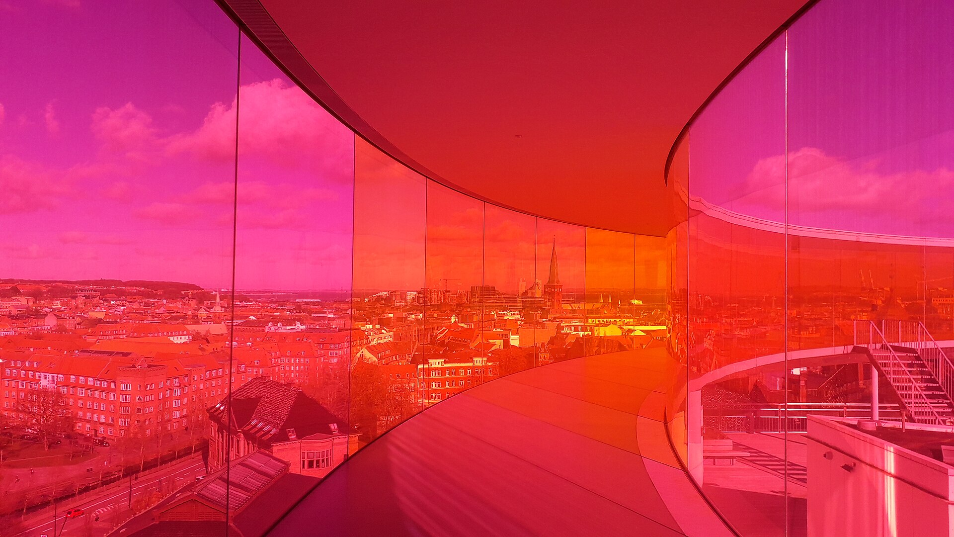 Inside the curved pink and orange glass walkway of Your Rainbow Panorama at ARoS in Aarhus, overlooking the city.