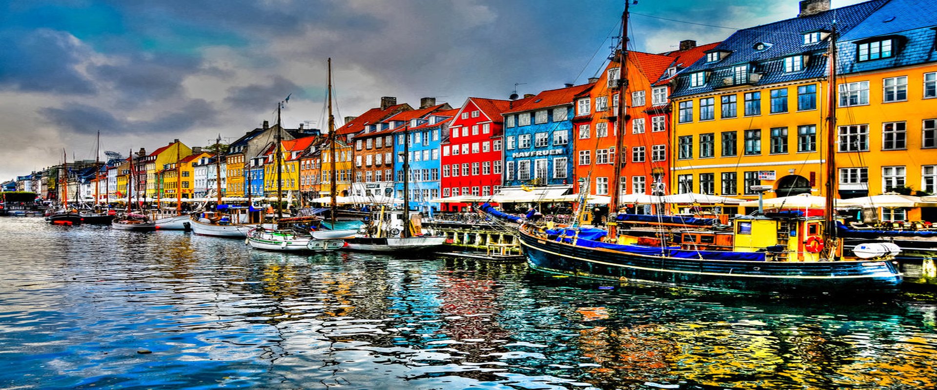 Colourful 17th-century townhouses lining the Nyhavn canal in Copenhagen at golden hour, with wooden sailing boats moored in front.